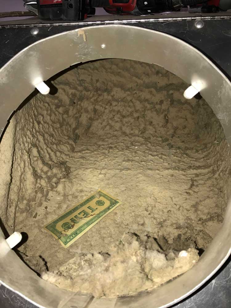 Inside of a dust-packed air duct with a ten dollar bill for scale