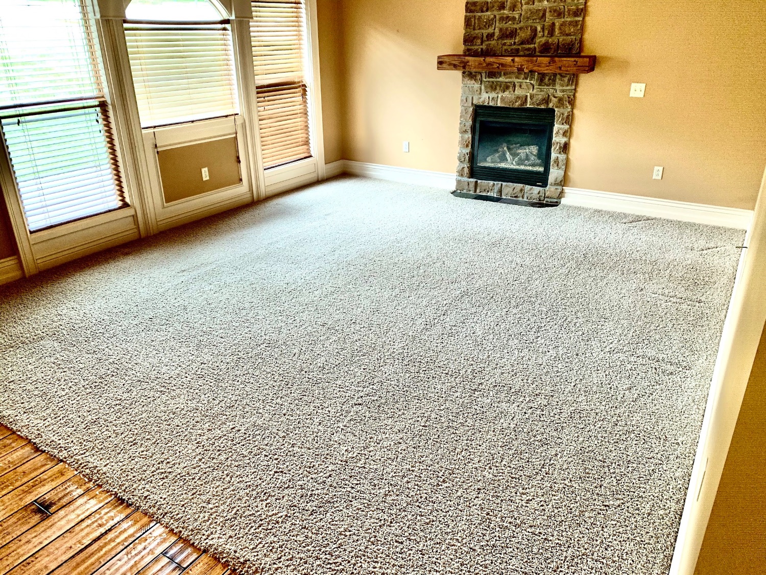 Living room with clean speckled carpet by a stone fireplace